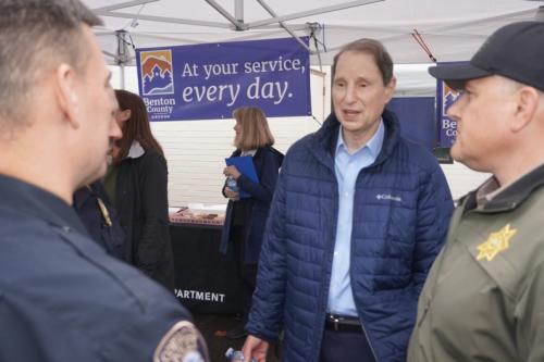 Man speaking to two men in law enforcement uniforms in front of a sign that says "At your service every day."