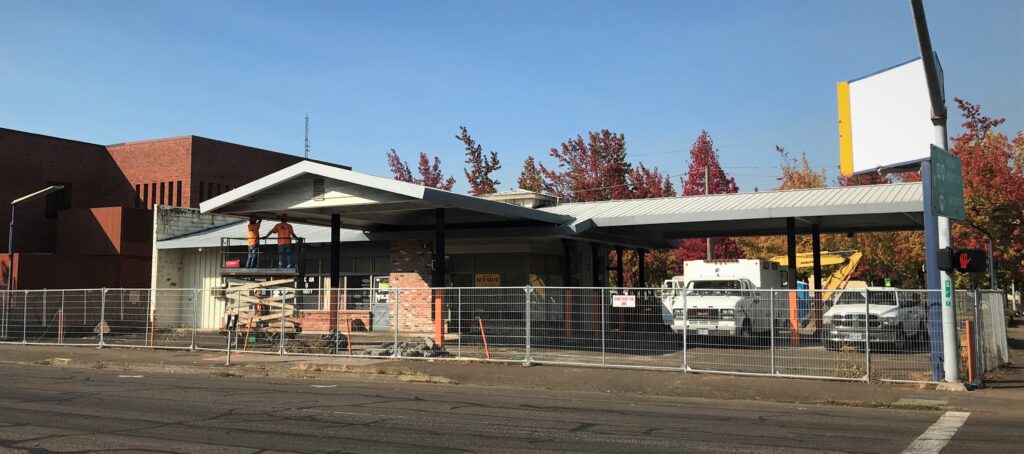 Two construction workers on lift equipment examine an old auto shop building to prepare it for demolition.