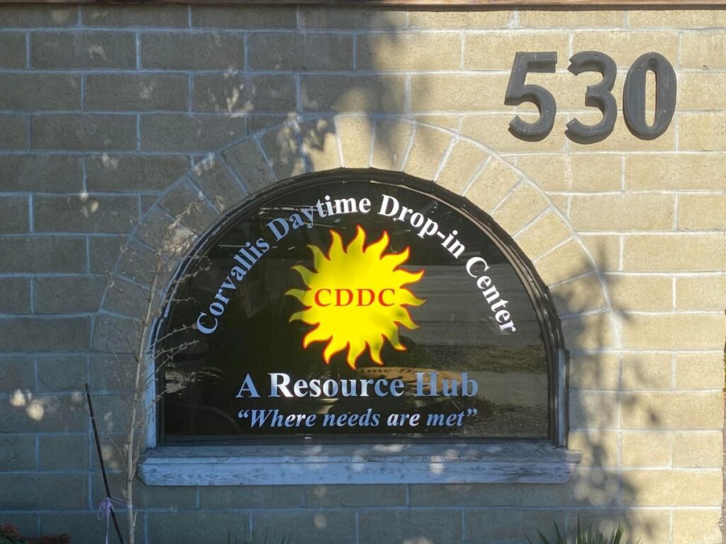 A window sign on a stone building with a yellow sun logo reads "Where needs are met."