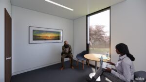 Two people sit across the table from one another in a room with a large window and artwork on the wall.