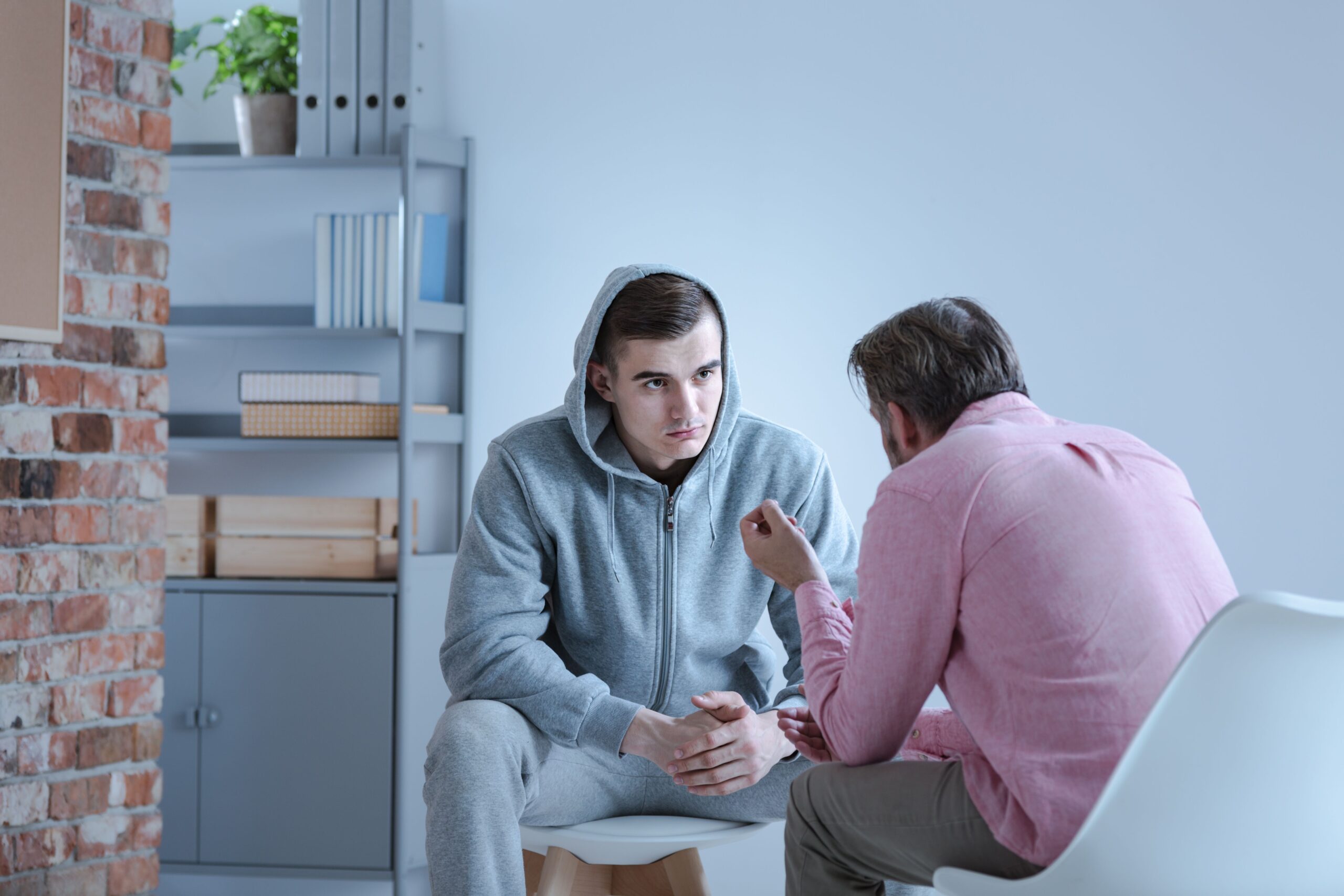 A middle age Caucasian man talks to a Caucasian teenaged boy wearing a grey sweat suit.