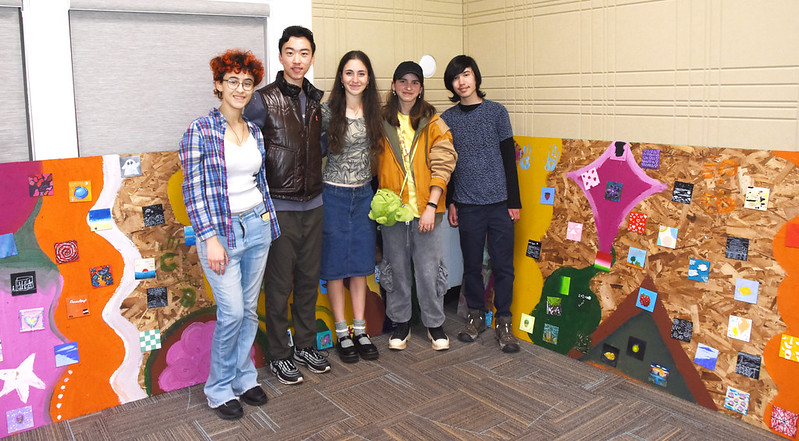 A group of teens pose in front of an art exhibit.