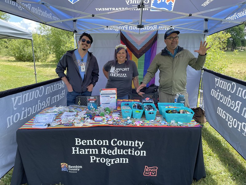 Three people standing behind a table of resource materials decorated with a pride flag.