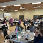 A large group of people sitting at round tables and clapping for people standing up.