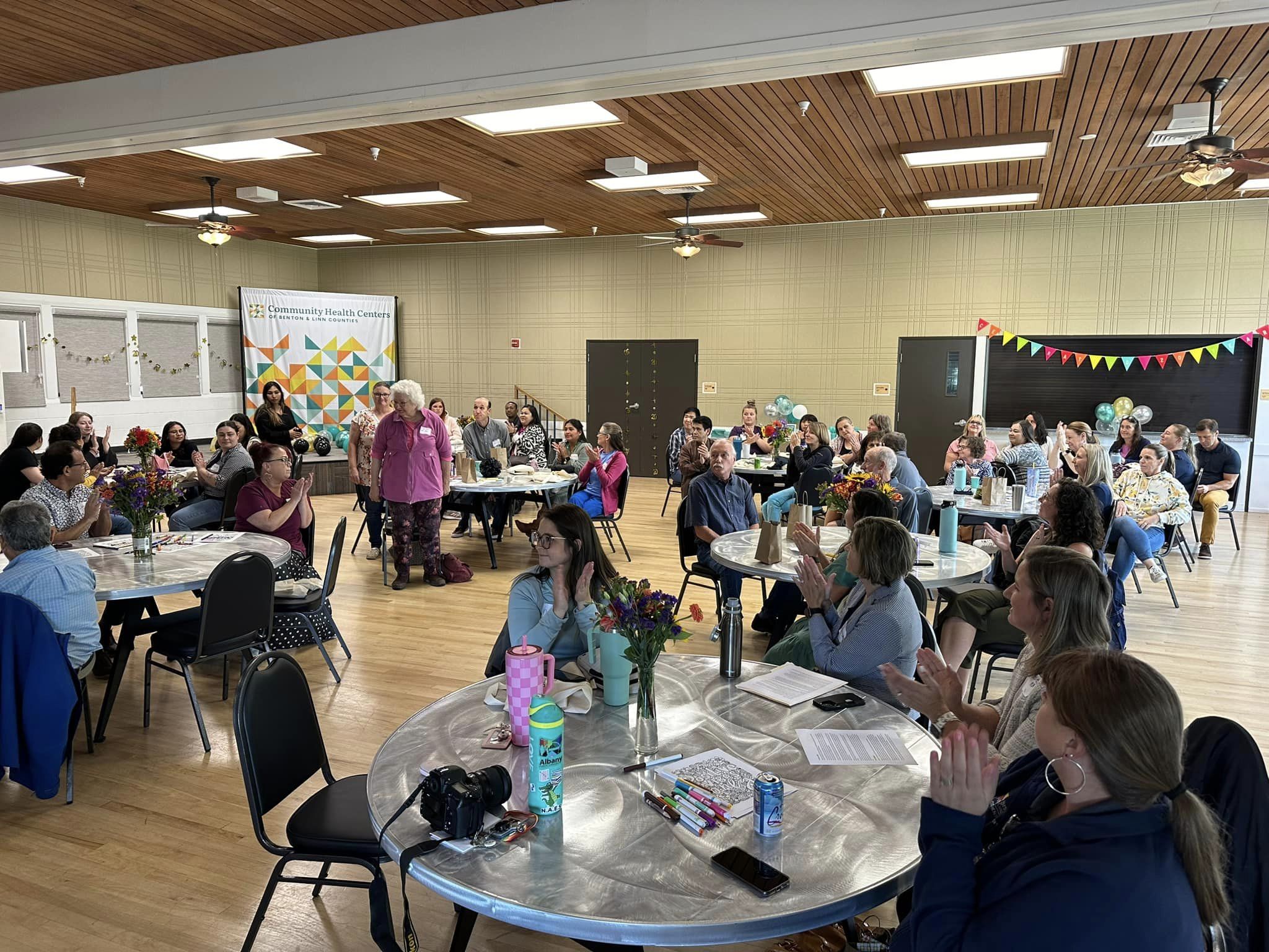 A large group of people sitting at round tables and clapping for people standing up.