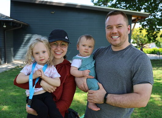 People holding two young children and smiling while outside.