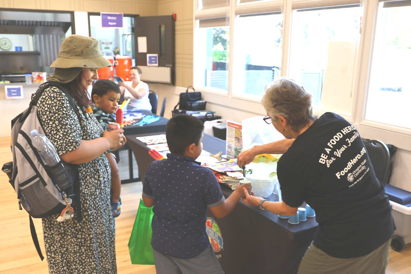 A woman and two children are assisted with a drink dispenser by another woman.