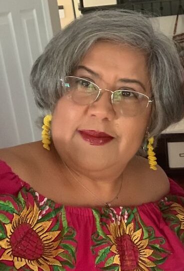 A Latina woman with short grey hair wearing a red top with sunflowers on it.