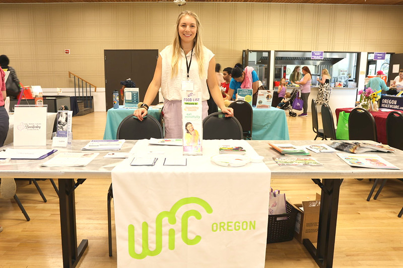 A woman stands behind a table that is covered in printed pamphlets and resource materials.