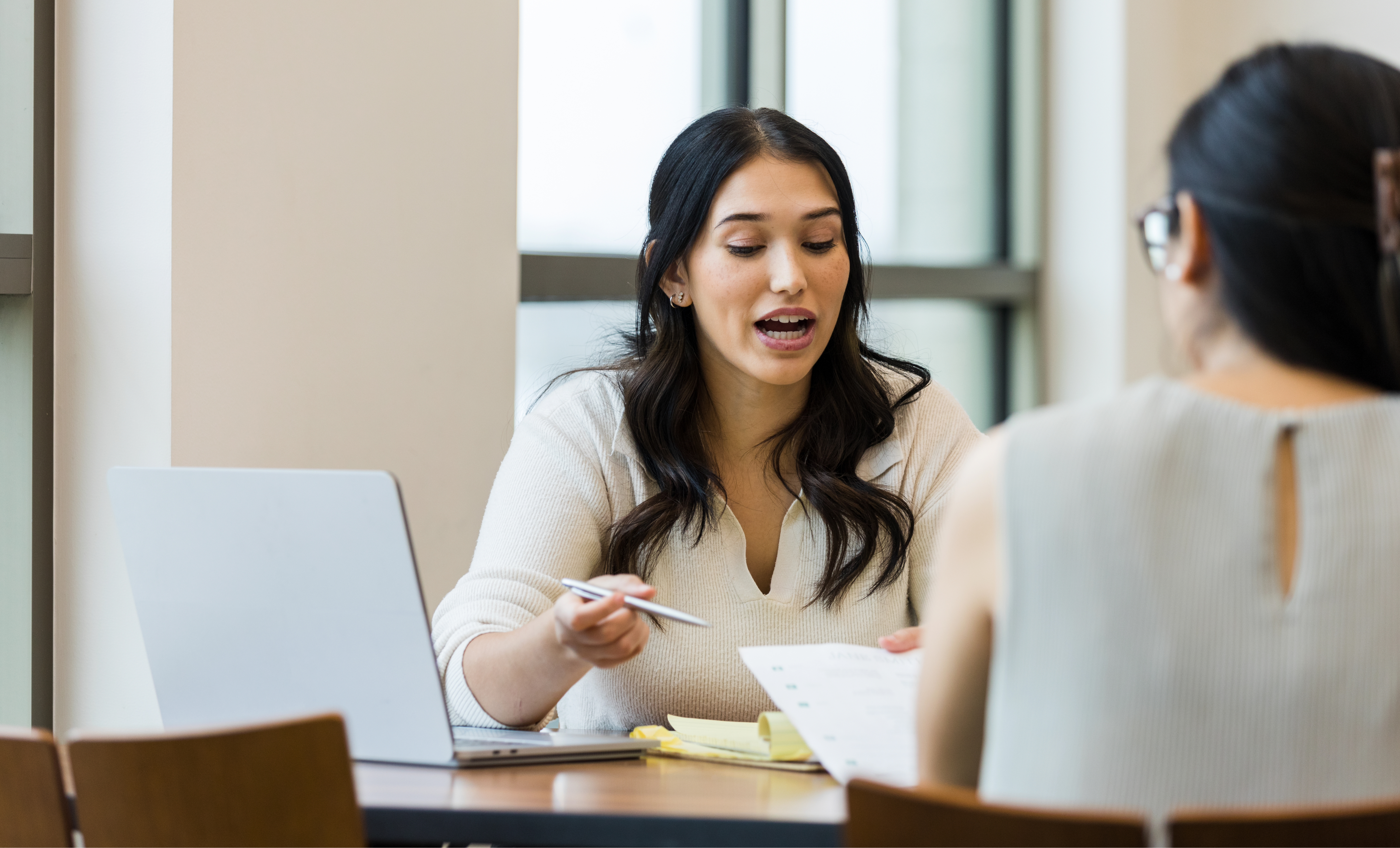 A woman passing a piece of paper across a desk to another person.