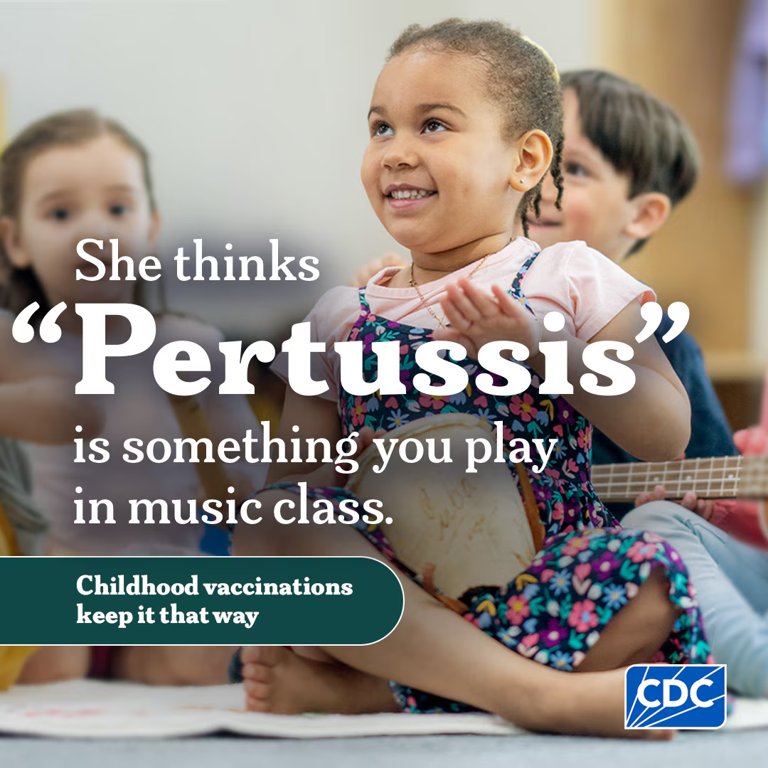 A young girl plays a drum in a classroom with other children.