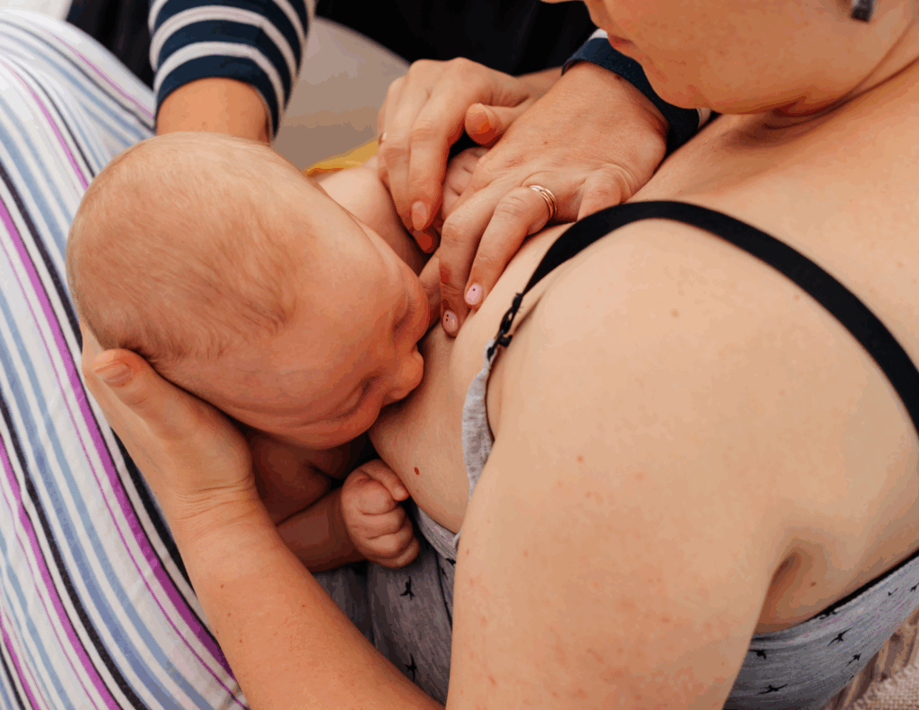 A baby breastfeeding while a lactation specialist helps with positioning.