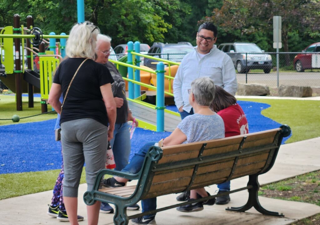 People smiling and visiting with each other near a bench at a park.