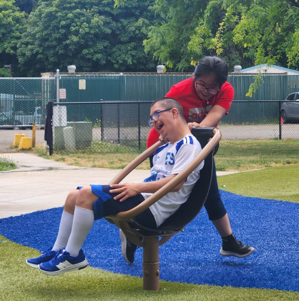 Two young people laughing and enjoying accessible playground equipment.