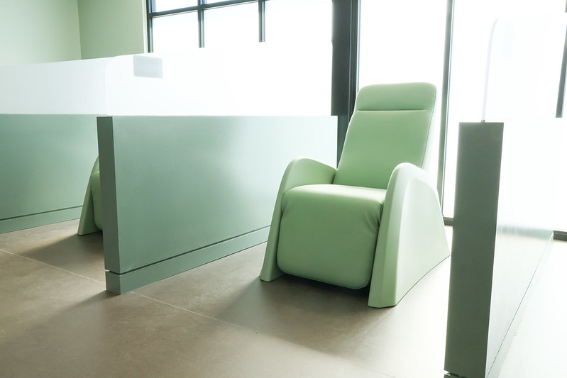 A pale green recliner in a sunlit room with large frosted windows and privacy dividers.