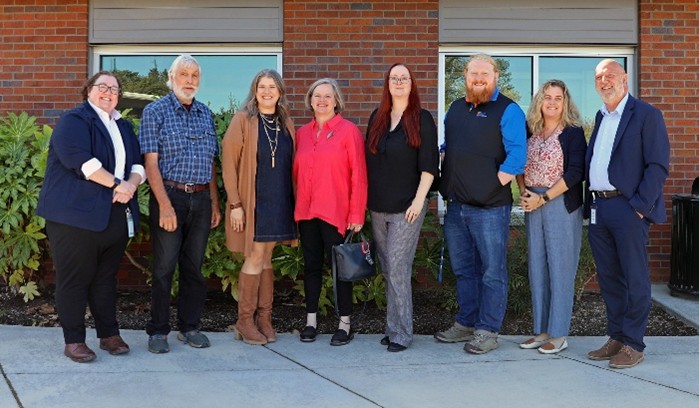 Eight clinic, county, and state leaders standing in front of brick building.