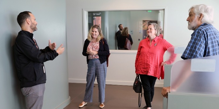 Four clinic and local leaders in interior crisis center building with sage color walls and mirror in the background.