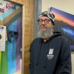 male standing in hallway with Crater Lake painting in the background and welcome sign.