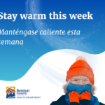 Person wearing an orange winter hat and gloves facing snowy hills under a blue sky with 'Stay warm this week' message.
