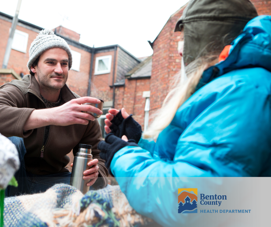 A person passes coffee to someone who is living on the street.