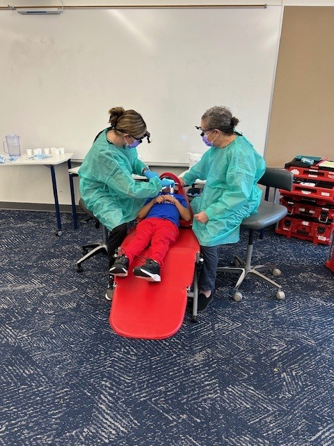 Dental staff work on a child patient in a classroom setting.