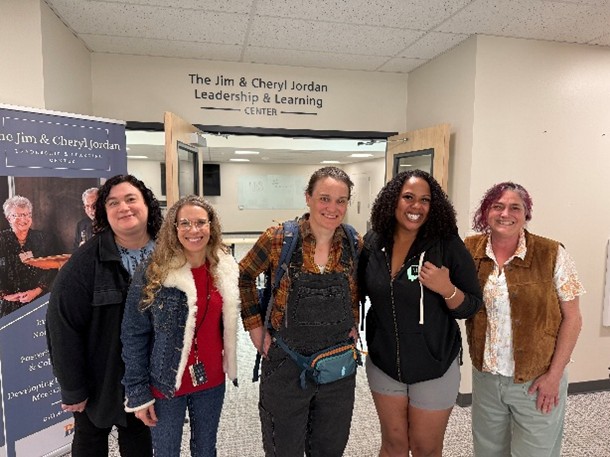 Five individuals stand together in a hallway beneath a sign for the Jim & Cheryl Jordan Leadership & Learning Center, with a display banner on the left and open double doors behind them.