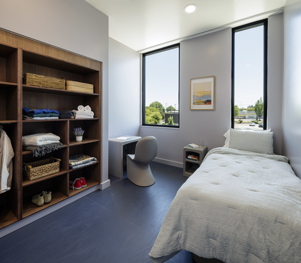 A badroom with a single bed, a small desk, and two windows.