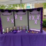 Memorial display with purple ribbons and candles honoring those lost to overdose on a purple-draped table under a tent.