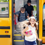 Children joyfully stepping off a yellow school bus with backpacks, water bottles and books.